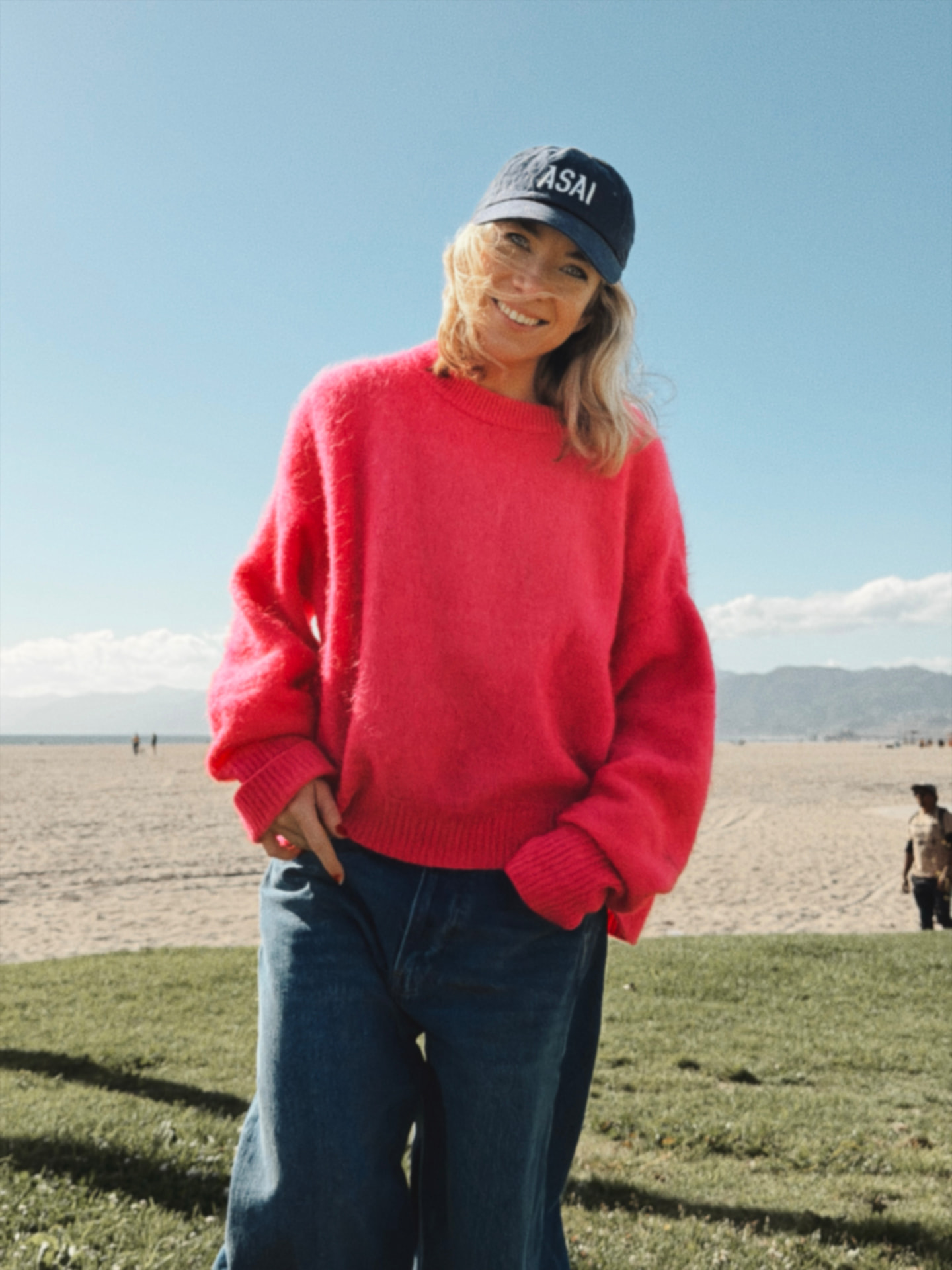 Frida, founder of Onuai, on a beach in a pink sweater and cap
